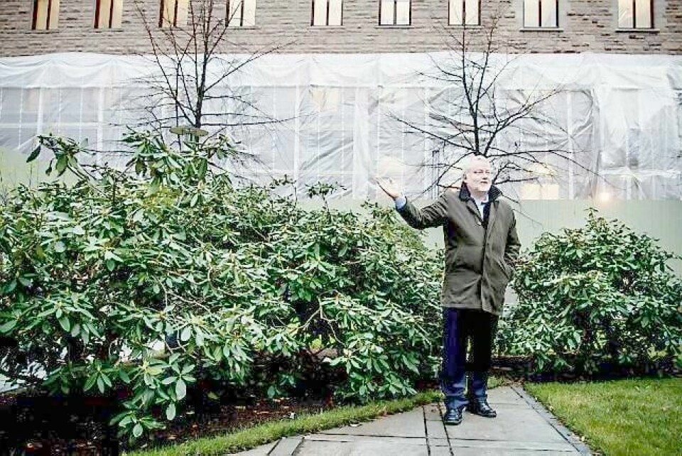Riksantikvar Jørn Holme, her med ryggen til Finansdepartementet, peker mot høyblokka som han vil frede. I dag feirer han riksantikvarembetets 100-årsdag.