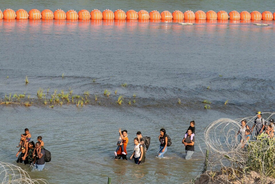 Migranter går mellom piggtråd og flytebøyer i Rio Grande på grensen mellom Mexico og USA. Flytebøyene er en del av en rekke tiltak fra Texas som skal motvirke ulvlig migrasjon til USA. Migranter går mellom piggtråd og flytebøyer i Rio Grande på grensen mellom Mexico og USA.