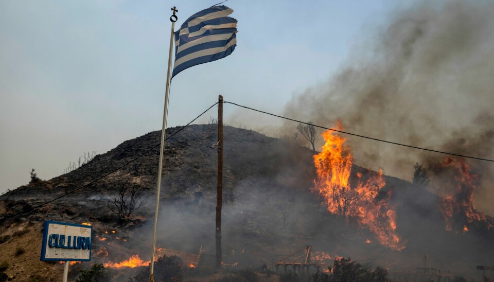 Et gresk flagg foran flammer på øya Rhodos mandag. Et gresk flagg foran flammer på øya Rhodos mandag. Foto: Petros Giannakouris / AP / NTB