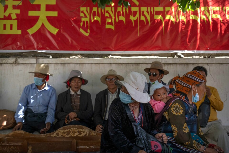 Tibetanere hviler seg under et regjeringsbanner der budskapet står både på tibetansk og kinesisk i Lhasa i Tibet. Bildet ble tatt i 2021 under en sjelden rundtur som ble arrangert for utenlandske journalister. Tibetanere hviler seg under et regjeringsbanner der budskapet står både på tibetansk og kinesisk i Lhasa i Tibet. Bildet ble tatt i 2021 under en sjelden rundtur som ble arrangert for utenlandske journalister. Foto: Mark Schiefelbein / AP / NTB
