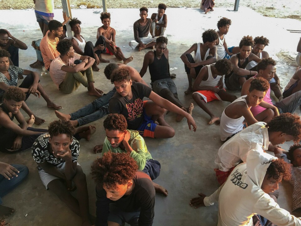 Rundt 30 unge menn som ble berget fra torsdagens forlis, sitter i skyggen på et betonggulv i Khoms. Kvinnene fikk hvile i en campingtilhenger etter å ha tilbrakt over seks timer i vannet. Rescued migrants sit on a coast some 100 kilometers (60 miles) east of Tripoli, Libya, Thursday, July 25, 2019. The U.N. refugee agency and the International Rescue Committee say up to 150 may have perished at sea off the coast of Libya. The country's coast guard says the Europe-bound migrants are missing and feared drowned after the boats they were traveling on capsized in the Mediterranean Sea. A spokesman says they rescued around 137 migrants on Thursday. (AP Photo/Hazem Ahmed)