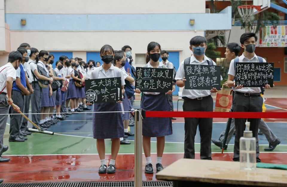 Skoleelever i Hongkong holder opp plakater med budskapet om at protestbevegelsens fem krav er ufravikelige.