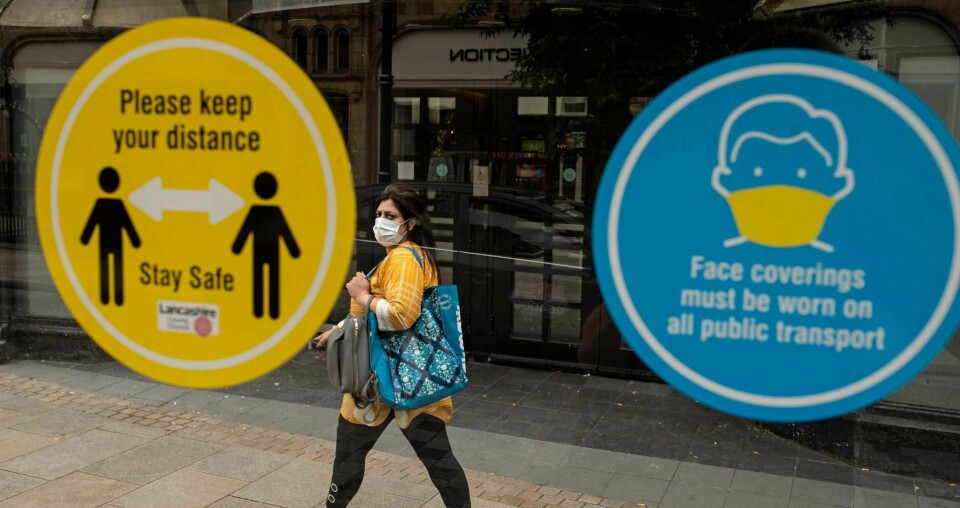Offentlig uthenging og skam kan være skadelig for smittevern på sikt, skriver Kaia Storvik. Her går en kvinne forbi skilt som ber folk holde avstand i byen Preston i Storbritannia, som har opplevd en økning i antall koronasmittede den siste tida. Foto: AFP/NTB scanpix