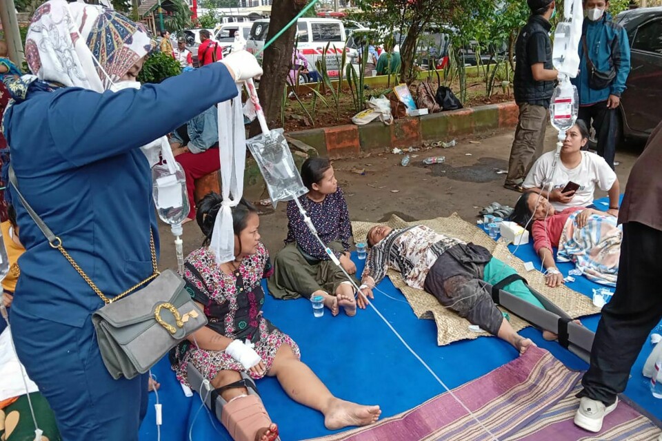 Skadde mennesker får medisinsk hjelp på en parkeringsplass ved et sykehus i Cianjur i Indonesia etter jordskjelvet som rammet landet mandag. Flere titalls mennesker er omkommet. People injured during an earthquake receive medical treatment in a hospital parking lot in Cianjur, West Java, Indonesia, Monday, Nov. 21, 2022. An earthquake shook Indonesia's main island of Java on Monday damaging dozens of buildings and sending residents into the capital's streets for safety. (AP Photo/Firman Taqur)