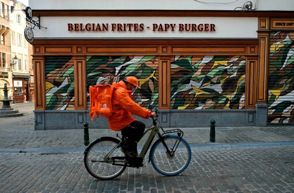 Et sykkelbud med munnbind sykler forbi en stengt restaurant i Brussel. Belgia har stengt det meste ned, og nå begynner det å gi resultater på smitte- og sykdomsgrafen.