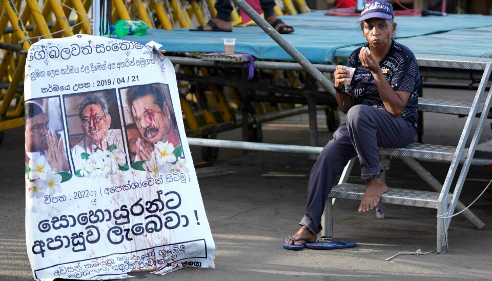 Sri Lankas president Gotabaya Rajapaksas oppsigelse er formelt godkjent. Her drikker en demonstrant en kopp te ved siden av en plakat med bilder av Rajapaksa og brødrene. Sri Lankas president Gotabaya Rajapaksas oppsigelse er formelt godkjent. Her drikker en demonstrant en kopp te ved siden av en plakat med bilder av Rajapaksa og brødrene. Foto: Eranga Jayawardena / AP / NTB