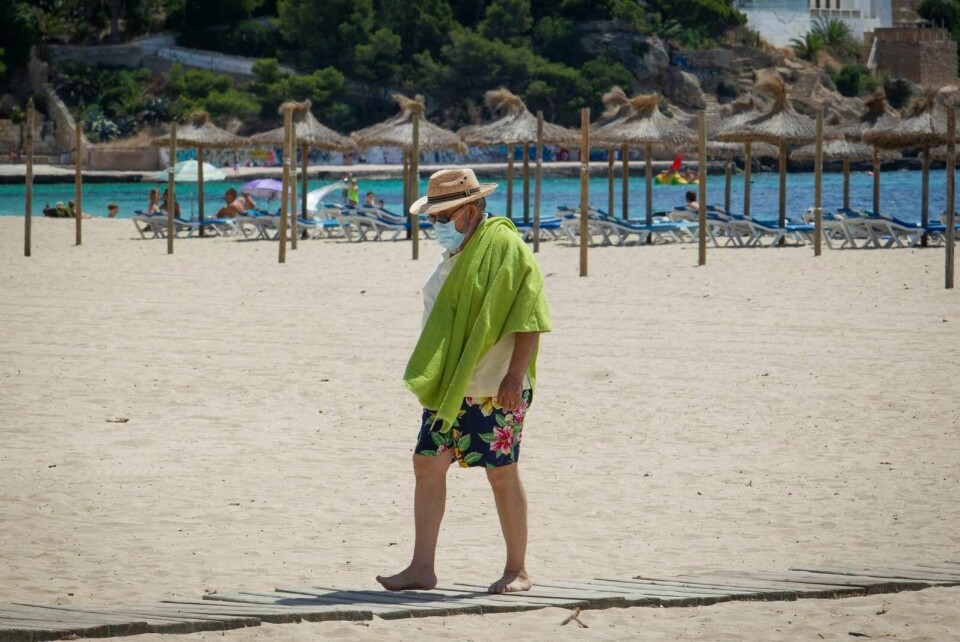 En turist med ansiktsmaske spaserer på Magaluf Beach i Calvia på Mallorca. Foto: Jaime Reina/AFP