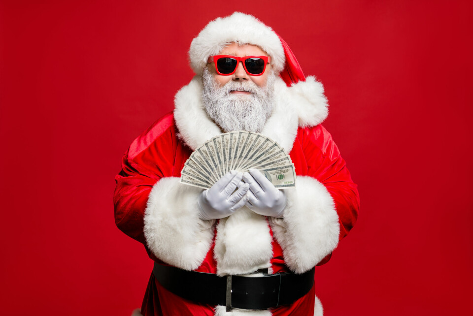 Julenissen jobber én dag i året, men er likevel en av verdens rikeste. Portrait of cool stylish elderly santa claus hipster millionaire have cash, want buy presents spend on winter season sales discount wear cap hat eyewear eyeglasses isolated over red background