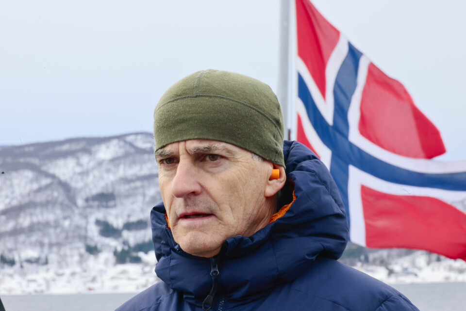 Statsminister Jonas Gahr Støre gratulerer med nasjonaldagen. Foto: Geir Olsen / NTB Bildet er av Jonas Gahr Støre. Han har på ytterjakke og en grønn lue. Han står foran et stort norsk flagg, og bildet er tatt utendørs. Det er fjell og fjord bak ham.Foto: Geir Olsen / NTB