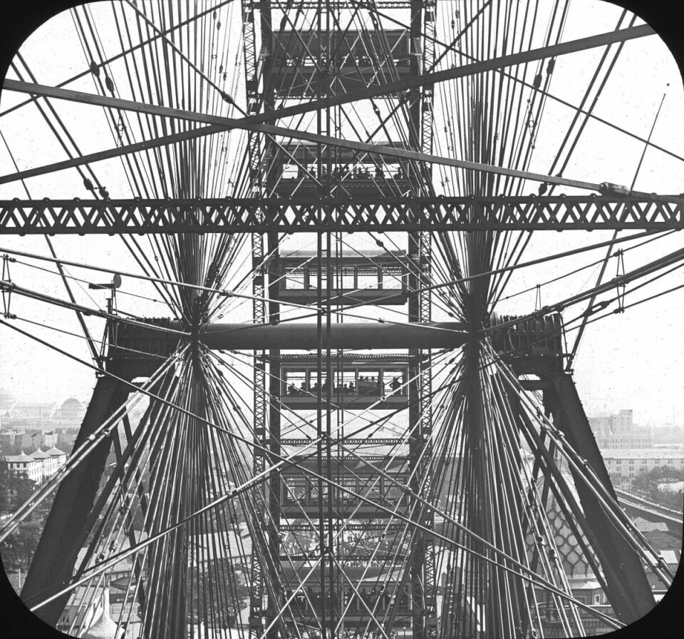 Utsikt mot akselen på verdens første pariserhjul.(Ukjent/Brooklyn museum/wikimedia commons) Det går stenger på kryss og tvers. Bak ses vogner med vinduer.