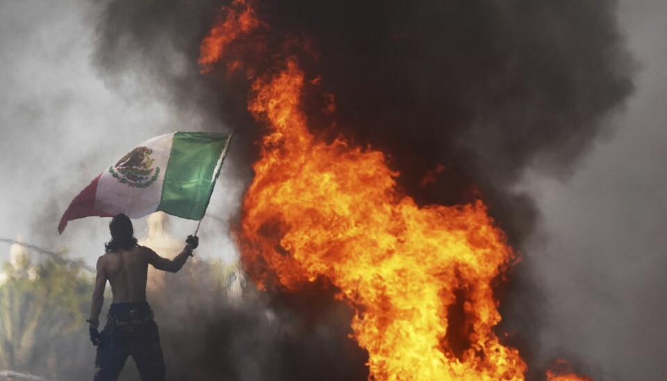 En demonstrant vifter med et mexicansk flagg foran en brennende selvkjørende drosje.