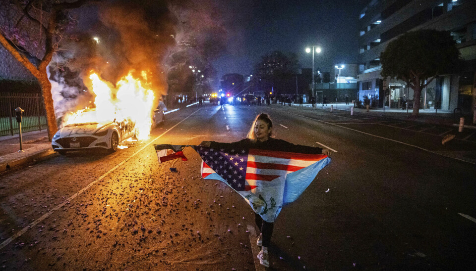En demonstrant viser fram både det amerikanske og mexicanske flagget mens hun går forbi en brennende bil i Los Angeles.