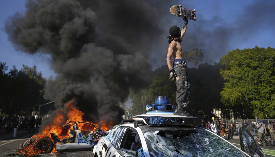 En demonstrant foran en brennende drosje i sentrum av Los Angeles.